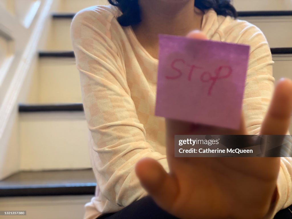 Unrecognizable mixed-race teen girl holds up note with the word “stop”