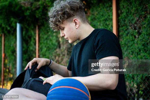 young basketball player sitting on the bench - basketball sideline stock pictures, royalty-free photos & images