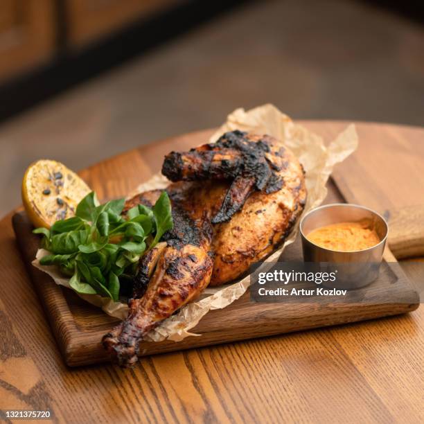 half of baked chicken with basil and sauce on wooden cutting board. appetizing lunch for loved one. hearty snack. soft focus. square format - halved chicken stock pictures, royalty-free photos & images