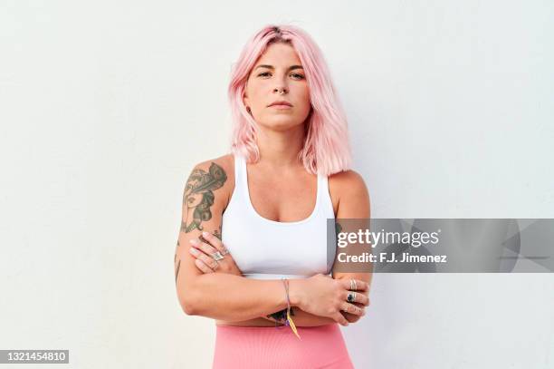 portrait of woman with pink hair with crossed arms in front of white wall - tattooing stock-fotos und bilder