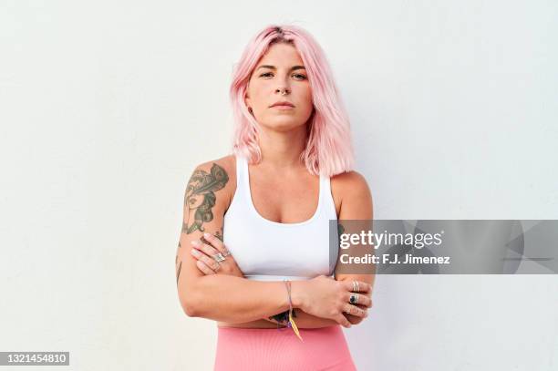 portrait of woman with pink hair with crossed arms in front of white wall - braços cruzados mulher imagens e fotografias de stock