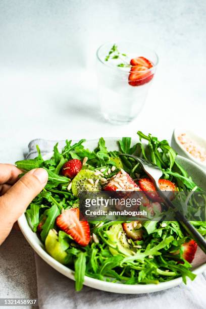 close-up of a woman eating a bowl of rocket, strawberry and kiwi fruit salad with sunflower seeds and chia seeds - sonnenblumenkerne stock-fotos und bilder