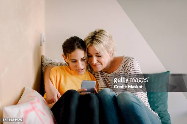 mature woman sitting with daughter using smart phone in bedroom at home - junior high age stock pictures, royalty-free photos & images