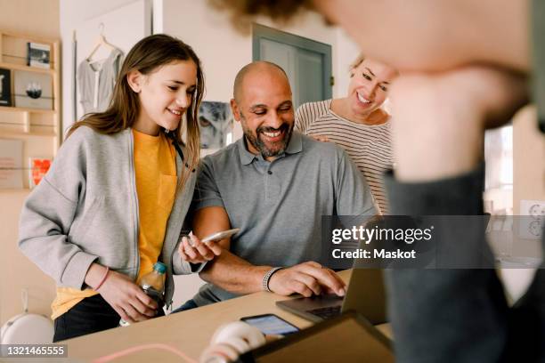 smiling woman and daughter looking at man doing online shopping at home - family teenager home life stock pictures, royalty-free photos & images