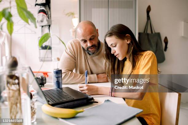 father assisting daughter doing homework at home - hausaufgaben stock-fotos und bilder