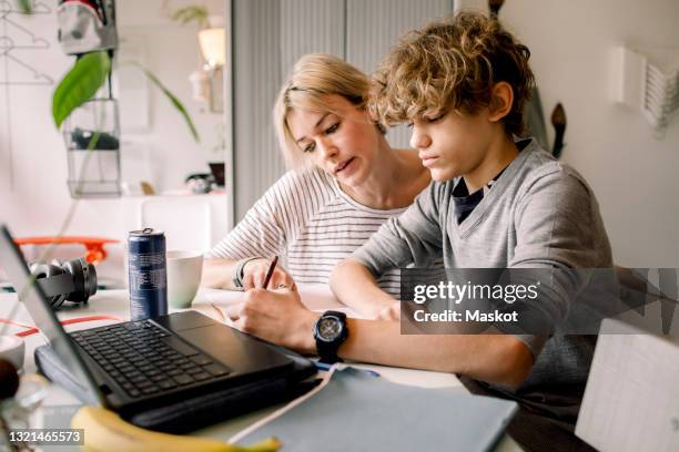 mother guiding son doing homework while sitting at table - huiswerk stockfoto's en -beelden