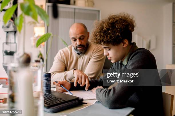 father guiding son doing homework while sitting at table - homework help stock pictures, royalty-free photos & images