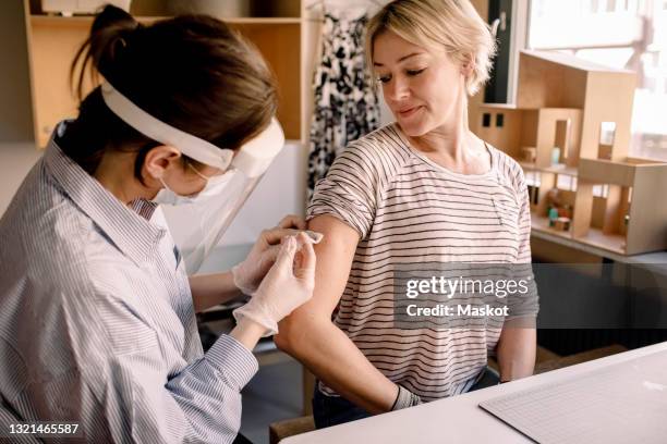 female nurse injecting medicine to blond woman at home - face shield stock-fotos und bilder