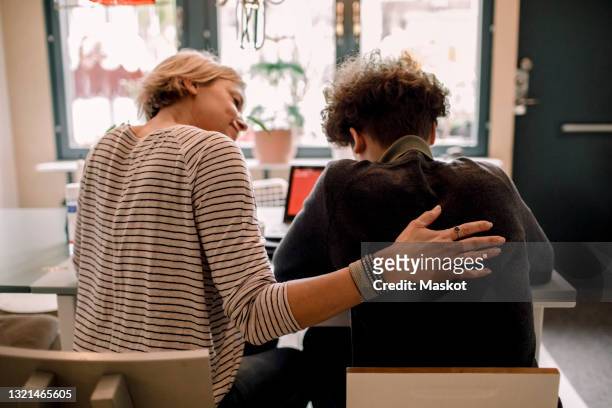 mother sitting by teenage son studying at home - assistance stockfoto's en -beelden