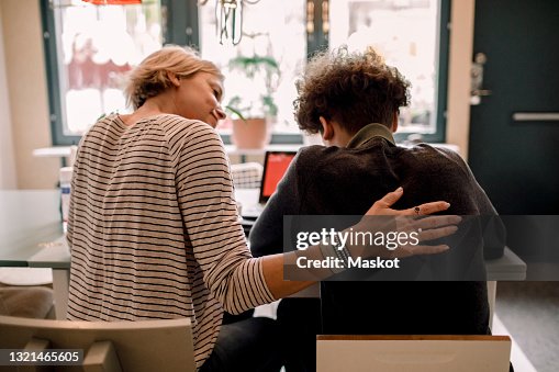 Mother sitting by teenage son studying at home Mother sitting by teenage son studying at home