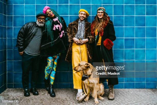full length of smiling men and women with dog against blue wall - fashion stock-fotos und bilder