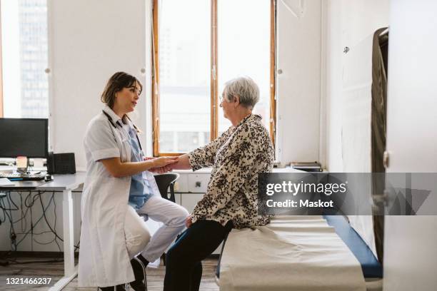 female doctor checking pulse of senior patient at medical clinic - hausarzt stock-fotos und bilder
