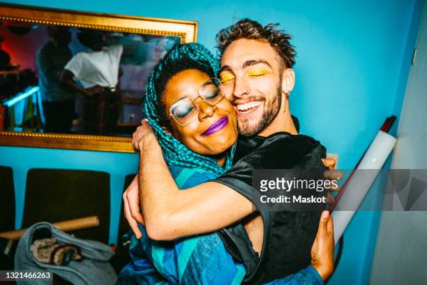 Happy male and female hipster friends hugging each other in living room