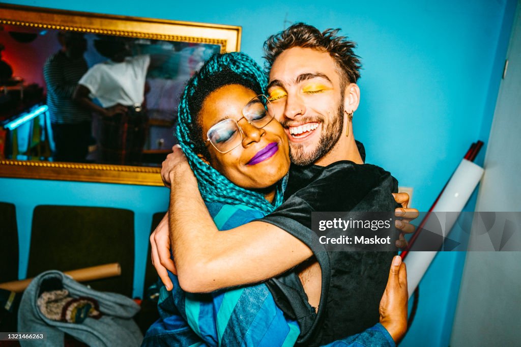 Happy male and female hipster friends hugging each other in living room
