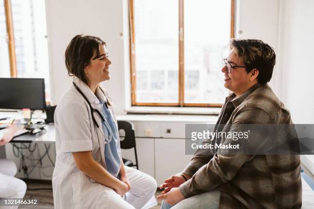 smiling female doctor and male patient discussing while consulting at medical clinic - male doctor man patient fotografías e imágenes de stock