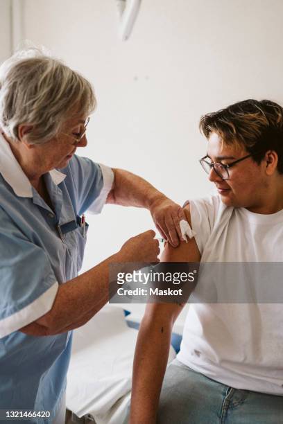 senior female doctor injecting male patient at medical clinic - injecteren stockfoto's en -beelden