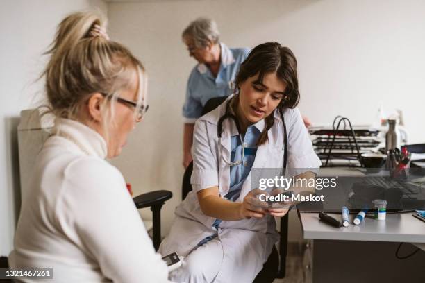 female healthcare worker discussing over glaucometer with patient in medical clinic - glaucometer stockfoto's en -beelden