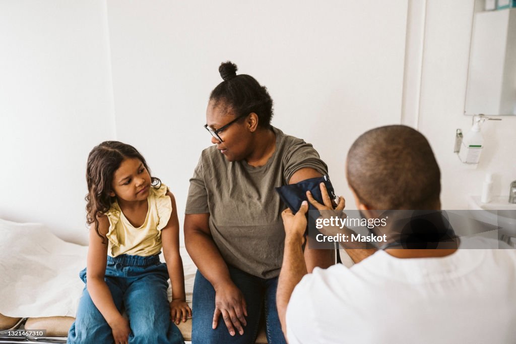 Mother talking with daughter while male doctor measuring blood pressure