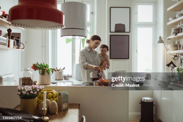 female professional pouring coffee while carrying toddler son in kitchen - in ear headphones photos et images de collection