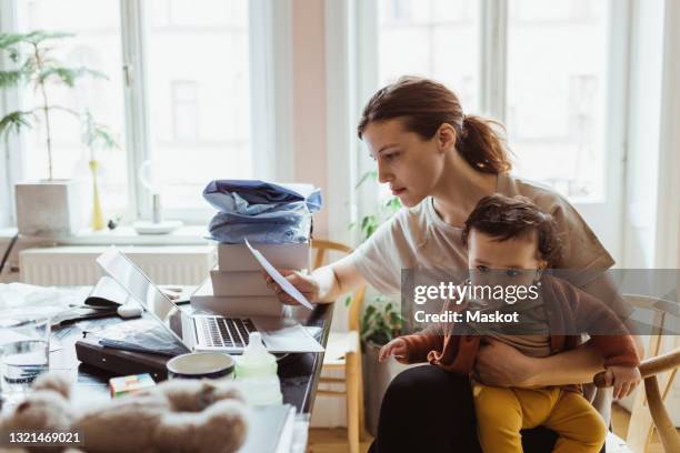 businesswoman reading document while sitting with baby boy in living room - budget bildbanksfoton och bilder