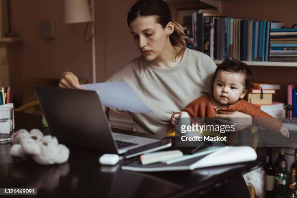 female professional reading document while sitting with male toddler at home - madre soltera fotografías e imágenes de stock