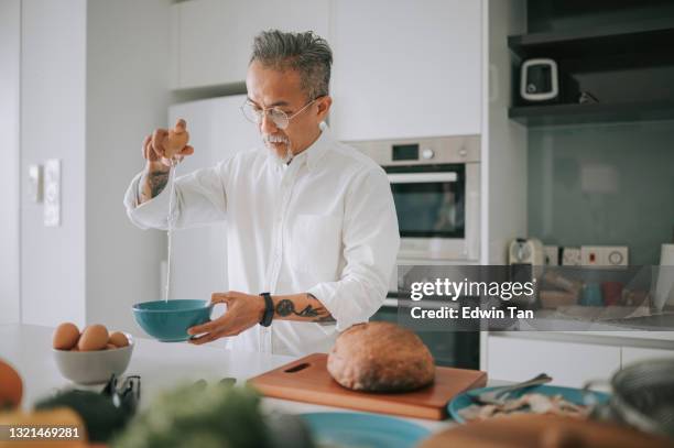 asian chinese gray hair senior man hair stubble cracking eggs preparing food cooking at home kitchen weekend - breaking bread stock pictures, royalty-free photos & images