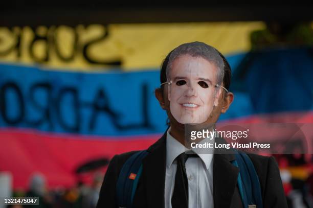 Demonstrator wearing a mask with a photo of president of Colombia Ivan Duque, poses in front of a Colombian flag on the background as thousands...