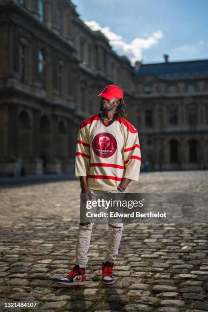 Cali Chiki wears a red Asos cap, a beige with red stripes sport t-shirt with Canada Nations Cup Hockey Tournament logo, white with multicolor paint...