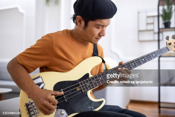 ソファに座って自宅のリビングルームでベースギターを弾く日本人男性 - エレキギター ストックフォトと画像
