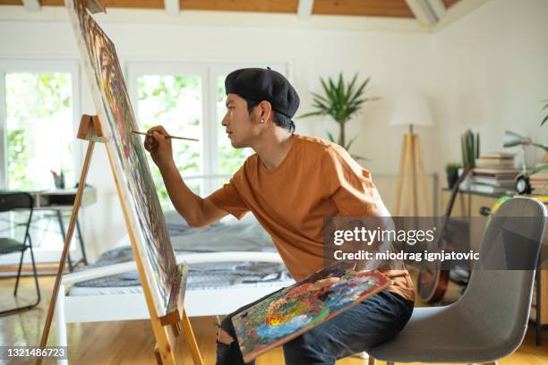 japanese man spending weekend morning painting in his bedroom at home - man painting on canvas stock pictures, royalty-free photos & images