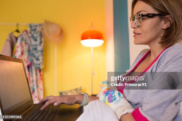 kvinnlig person som arbetar hemifrån i sin säng med bruten arm - armbrott bildbanksfoton och bilder