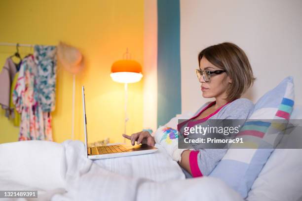 female person working from home in her bed with broken arm - broken arm stock pictures, royalty-free photos & images