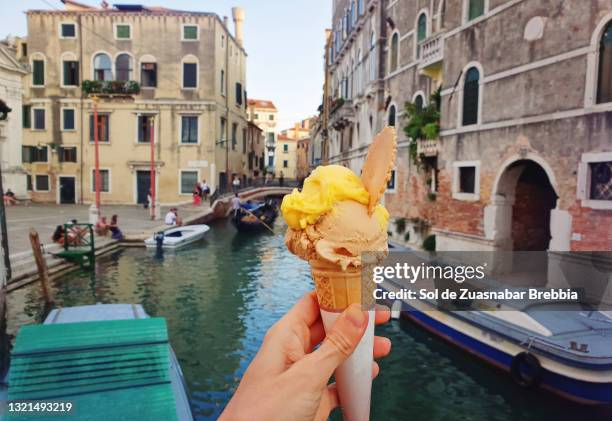 closeup of a refreshing sweet cone ice cream with a canal with its boats and houses behind - gelato fotografías e imágenes de stock