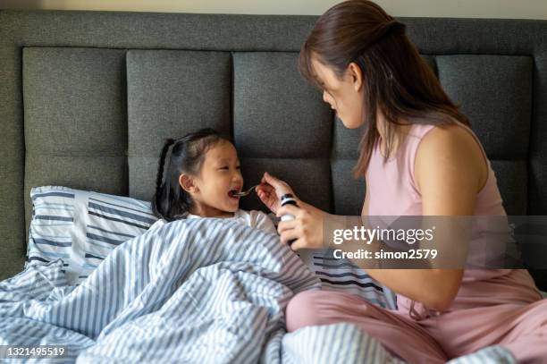 een aziatische moeder die hoeststroopgeneeskunde in duidelijke lepel aan haar dochter giet - allergy doctor stockfoto's en -beelden