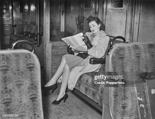 Fashion model Marie McGowan, wearing a fur lined coat, takes a London Underground tube train to work in the centre of town during World War II on 2nd...