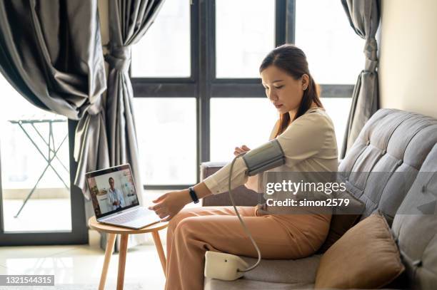 an asian woman on a video conference with her doctor checking her blood pressure at home - video reviewed stock pictures, royalty-free photos & images