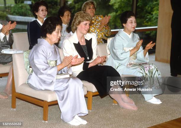 Diana, Princess of Wales, wearing a cream and black suit designed by Catherine Walker, sits barefoot while watching a demonstration of traditional...