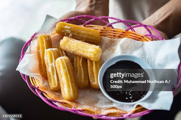 midsection of person holding plate os churros and chocolate sauce dip - churro stockfoto's en -beelden