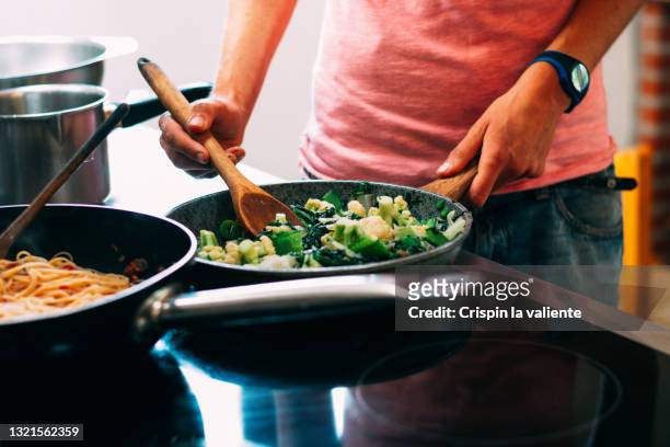 young woman cooking some vegetables in a frying pan on the ceramic hob in the kitchen - angebraten stock-fotos und bilder