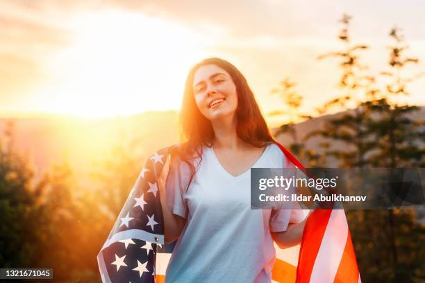 The concept of American National Holidays. A patriotic girl holds an American flag in her hands. Sunset in the background. Independence day