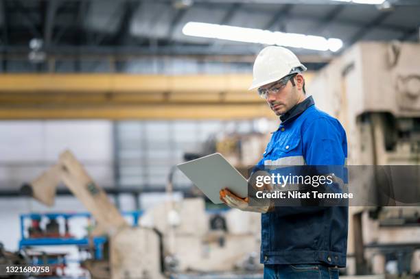 side view of production planning control engineer using laptop in front of stamping auto part hydraulics press machine while checking machinery capacity. production planning and control in automobile industry concepts. - civil engineering stock pictures, royalty-free photos & images