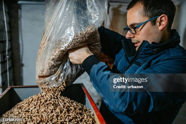 man pouring pellets in pellets boiler - biomass renewable energy source stock pictures, royalty-free photos & images