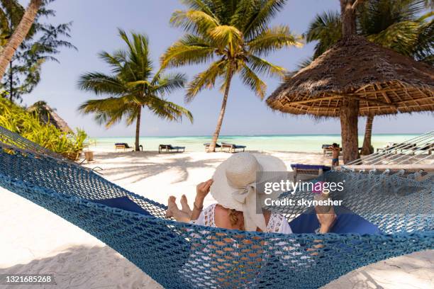 vista trasera de una mujer relajada con batido en hamaca en la playa. - zanzibar fotografías e imágenes de stock