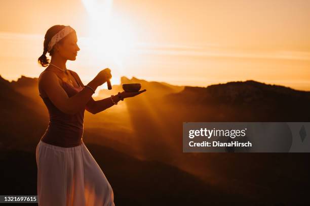 young woman doing meditation using a tibetan singing bowl during the sunrise in a mountainous landscape - gong stock pictures, royalty-free photos & images