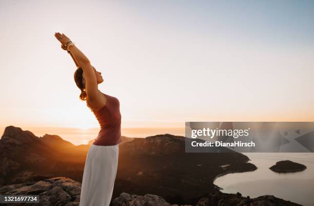 beautiful young woman doing the yoga upward salute urdhva hastasana position during the sunrise in a mountainous landscape - golden hour woman stock pictures, royalty-free photos & images