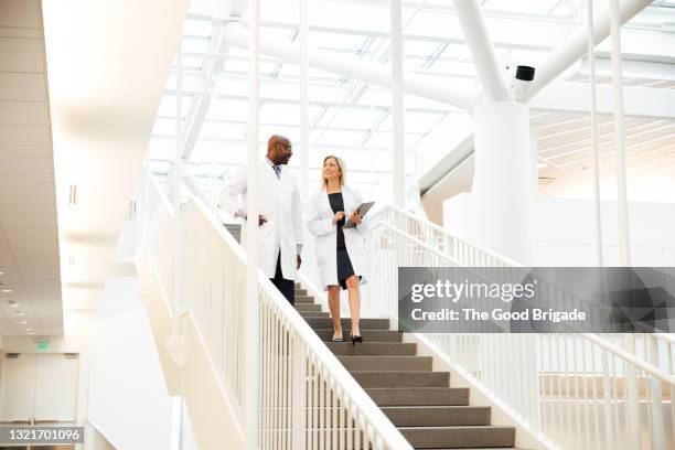 smiling female doctor talking to colleague on staircase in hospital - doctor looking down stock pictures, royalty-free photos & images