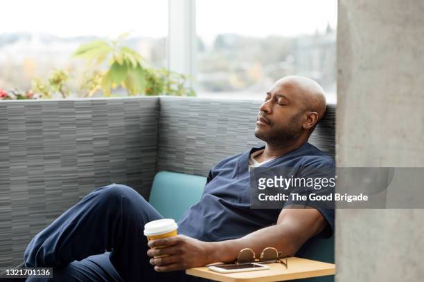 male nurse with disposable cup resting on sofa in hospital - relaxation stock pictures, royalty-free photos & images