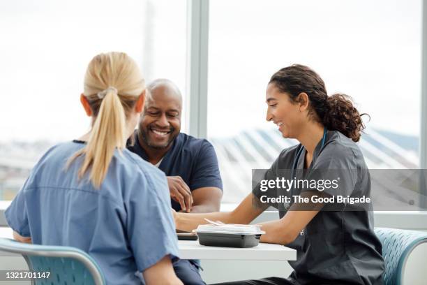 smiling male nurse talking to female colleagues in hospital cafeteria - lunch break stock pictures, royalty-free photos & images