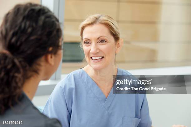 smiling female nurse talking to colleague in hospital - patientin stock-fotos und bilder