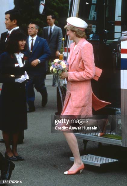 Diana, Princess of Wales, wearing a pink suit designed by Bruce Oldfield and a matching hat, holds a bouquet of flowers during a visit to the Nissan...